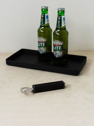 Trend{ING}s Stylish Leather Bottle Opener next to a black steel tray with two bottles of castle lite