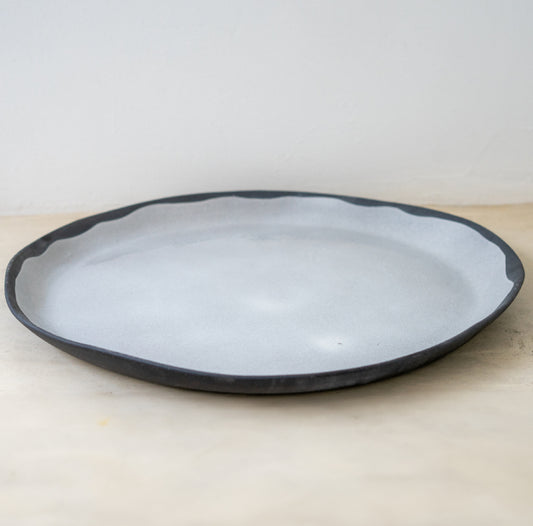 Trend{ING}s elegant XL Acacia flat ceramic platter. lying flat on a surface with a dark grey rim