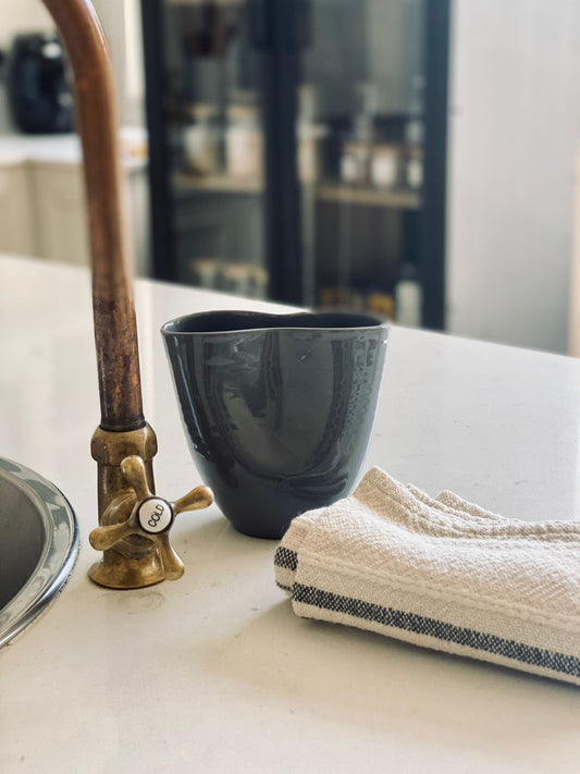 Trend{ING}s Ritual Cup & Towel in a charcoal colour next to a kitchen tap and the hand towel beside it