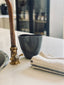 Trend{ING}s Ritual Cup & Towel in a charcoal colour next to a kitchen tap and the hand towel beside it