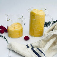 Trend-ings Glass measuring kitchen beaker 300 & 500ml sizes with a linen towel and juice in the beakers