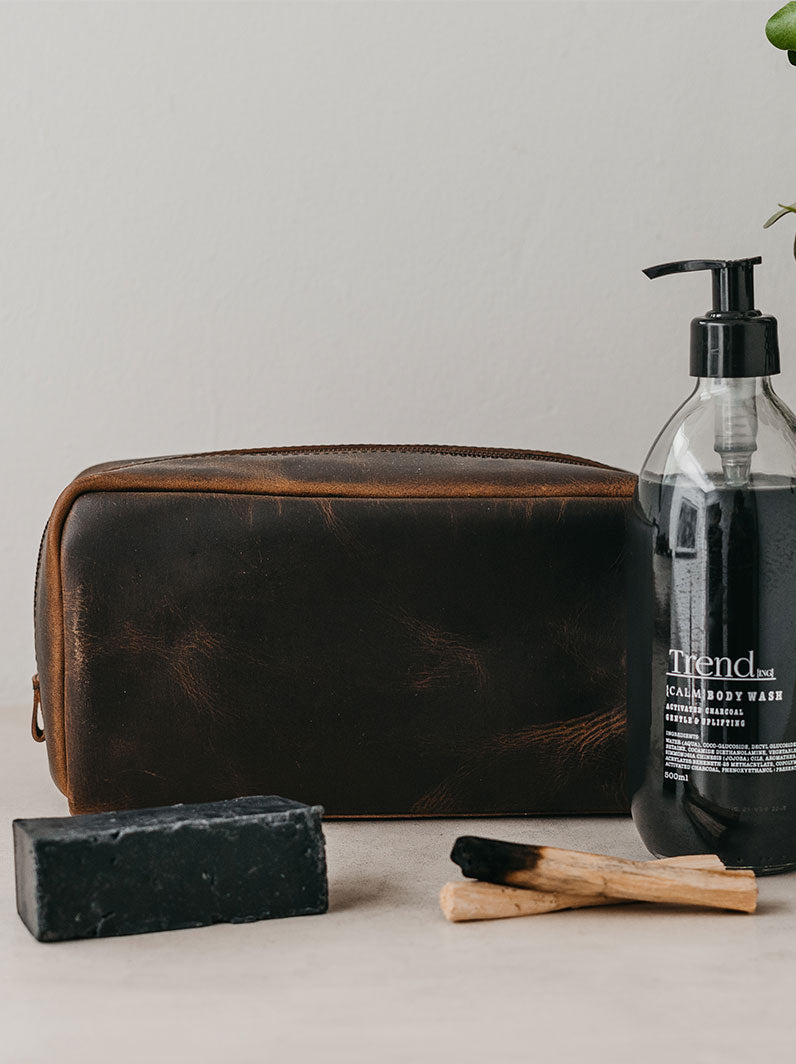 Trend-ing's Weathered leather cosmetic bag in brown with charcoal body wash and palo panto sticks beside it