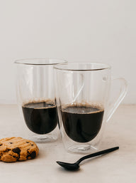 Trend-ings Modern glass coffee mugs; with espresso in them and a choc chip cookie and black metal spoon beside it