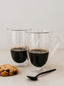 Trend-ings Modern glass coffee mugs; with espresso in them and a choc chip cookie and black metal spoon beside it